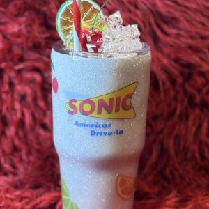 Glittery Sonic-inspired tumbler with faux ice, cherry, lime, and striped straw on red plush background.