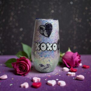 Iridescent glitter tumbler decorated with black hearts and 'XOXO', surrounded by roses and candies.
